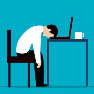 A man puts his head on a computer; he looks depressed or exhausted.
